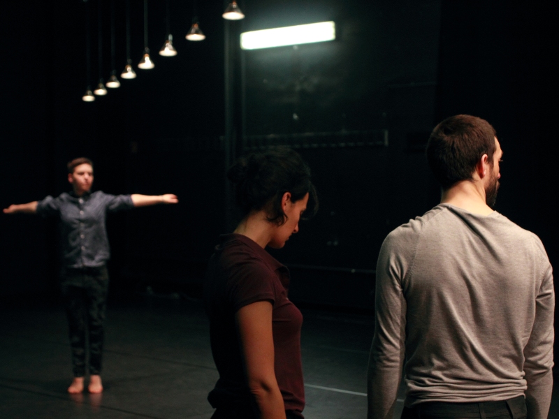 Drei Darsteller unter hängender Lichtreihe